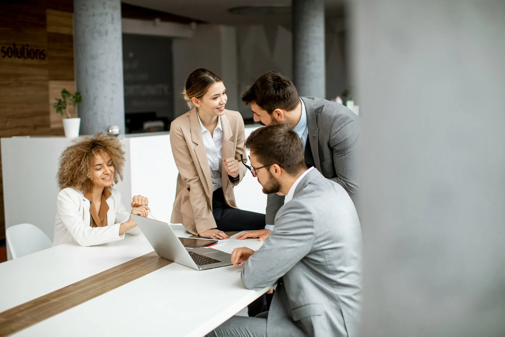 Four colleagues in business attire reviewing a deal around a laptop in an office